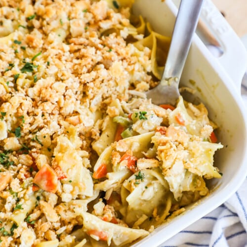 A spoon scoops out a serving of Chicken Noodle Casserole from a white casserole dish.