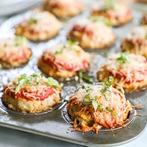 Chicken Parmesan Meatloaf Muffins with basil on top, in a muffin pan.