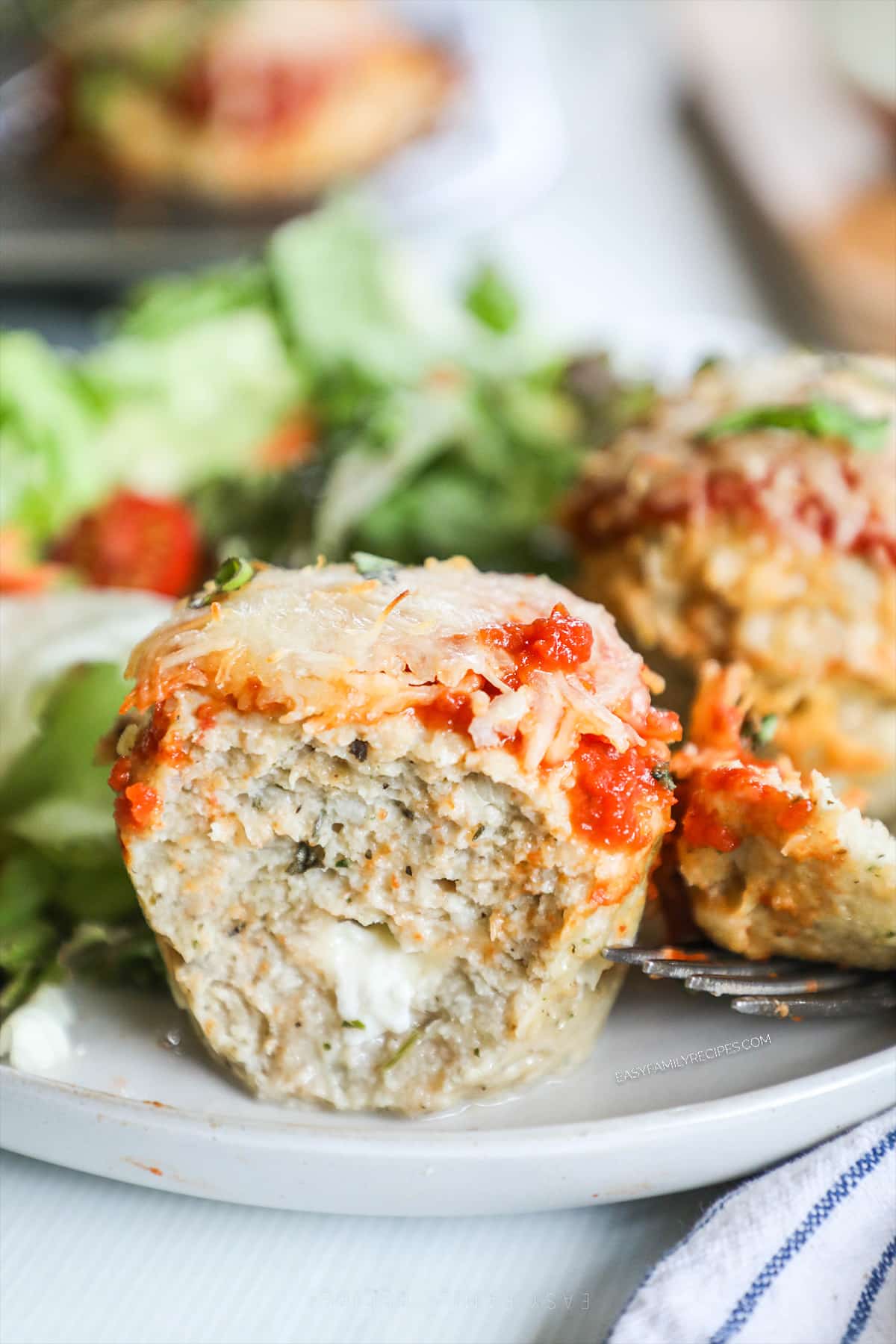 A side view of Chicken Parmesan Meatloaf Muffins on a white plate with a green salad.