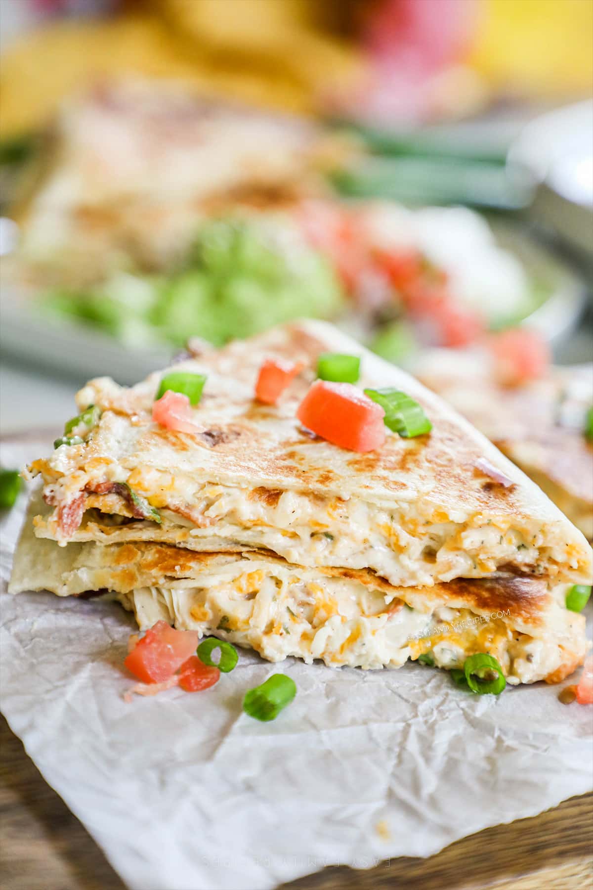 Two wedges of Chicken Bacon Ranch Quesadillas on a piece of white parchment paper with red peppers and scallions for garnish.