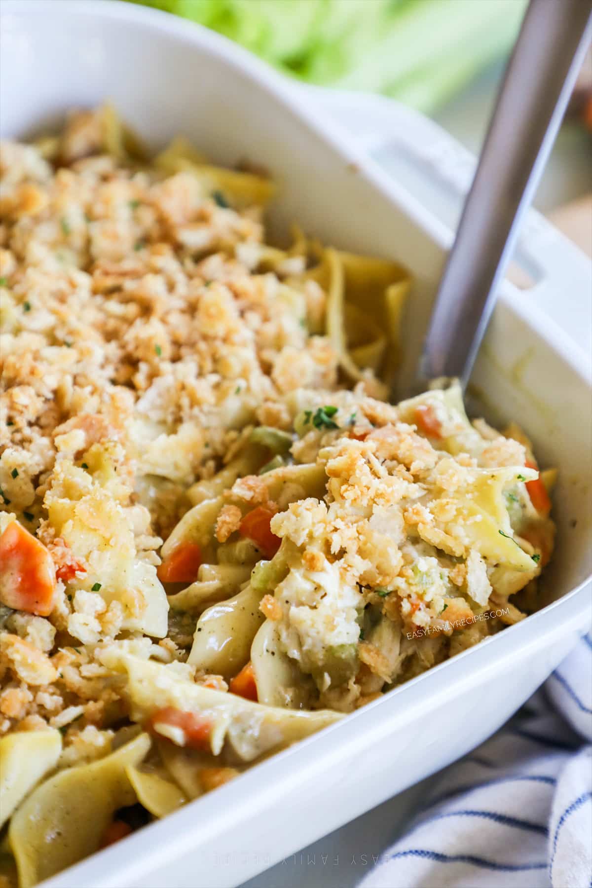 A spoon scoops out a serving of Chicken Noodle Casserole from a white casserole dish. 