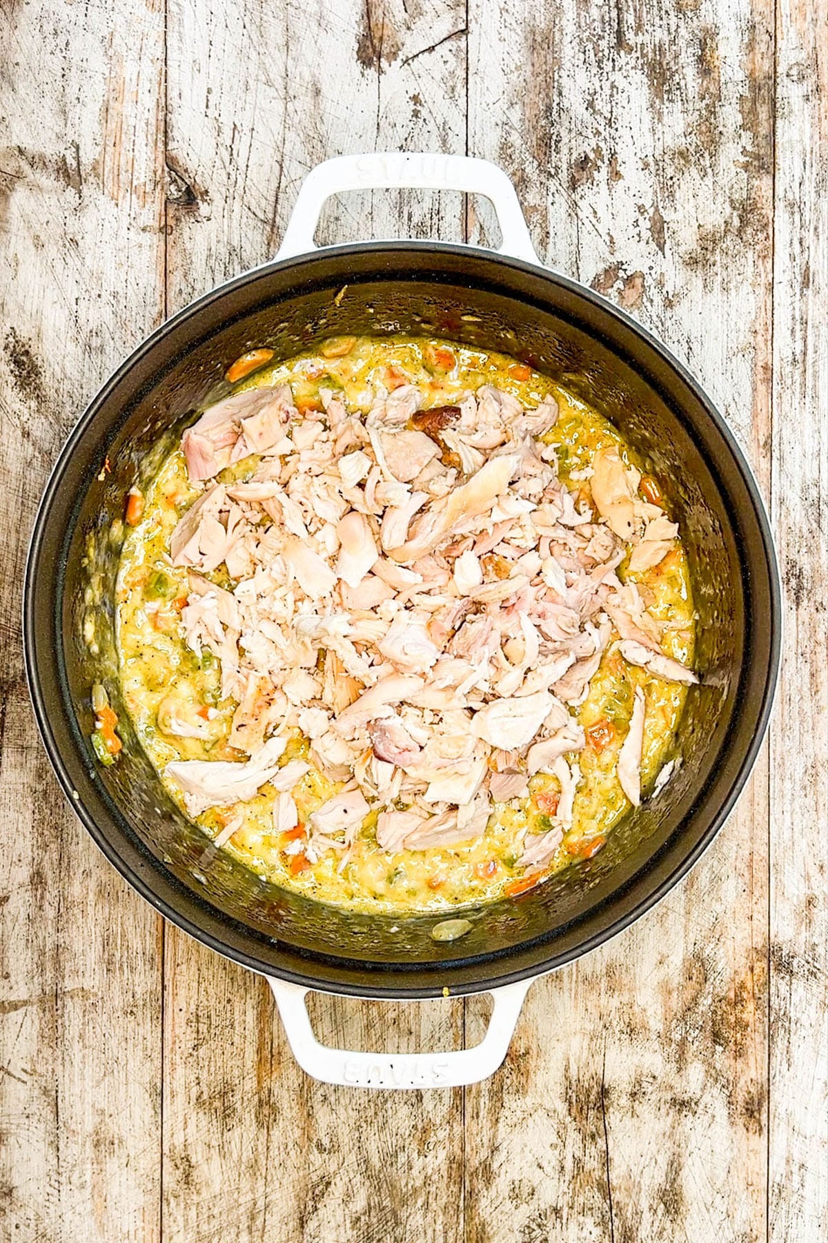 A skillet with the creamy veggies and chicken being mixed into for Chicken Noodle Casserole.