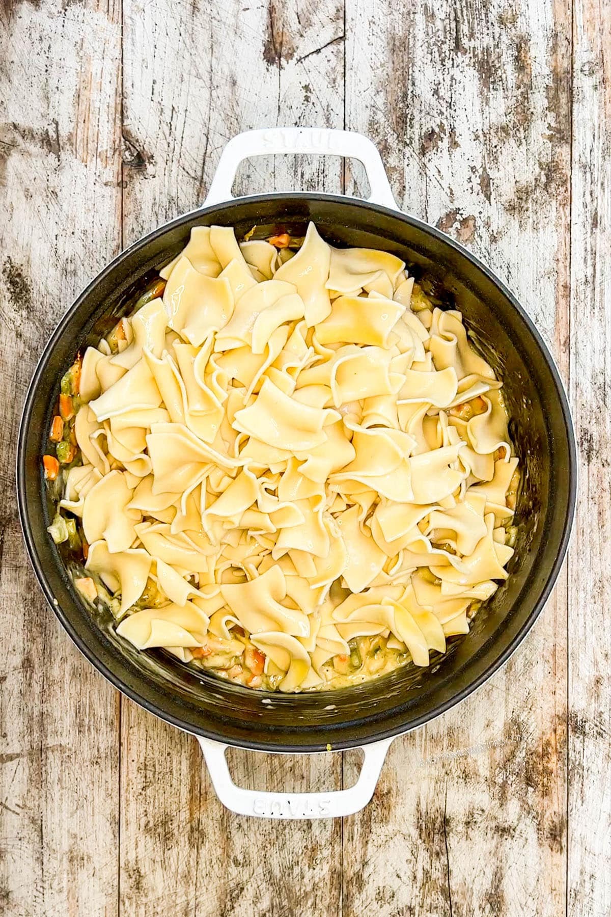 A black cast iron pan with the cooked noodles being mixed in for Chicken Noodle Casserole