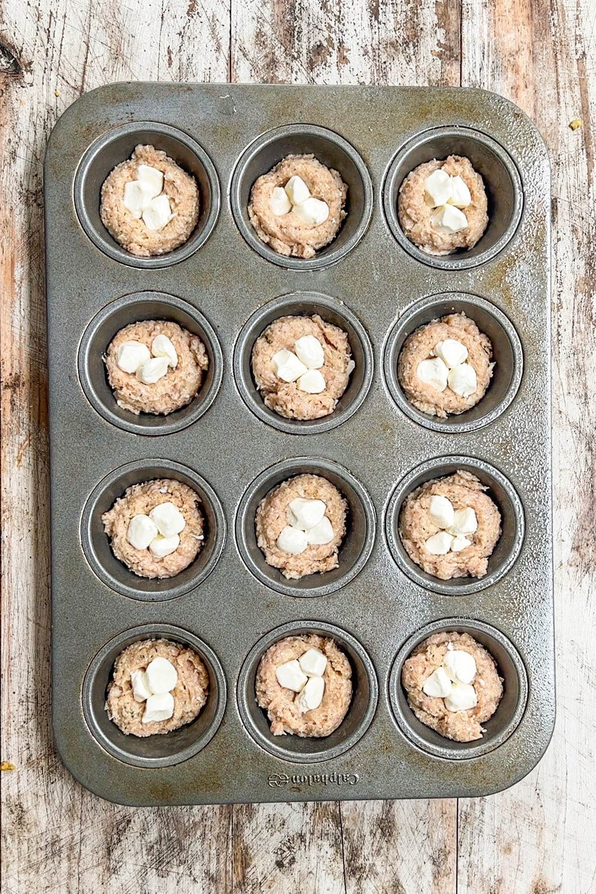 A top view demonstrating stuffing Chicken Parmesan Meatloaf Muffins with mozzarella cheese.