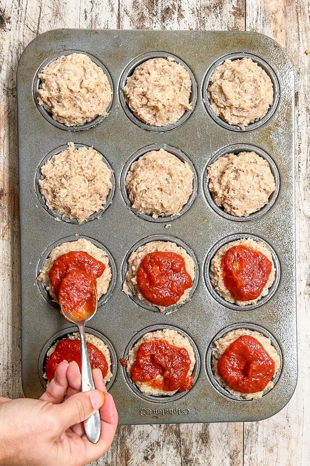 Adding marinara sauce to Chicken Parmesan Meatloaf Muffins.