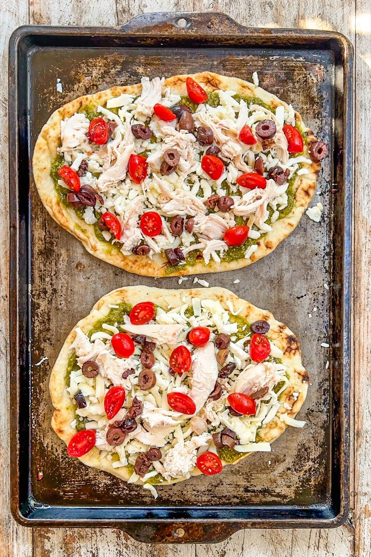 Two Mediterranean Chicken Flatbread pizzas being assembled on a baking sheet.