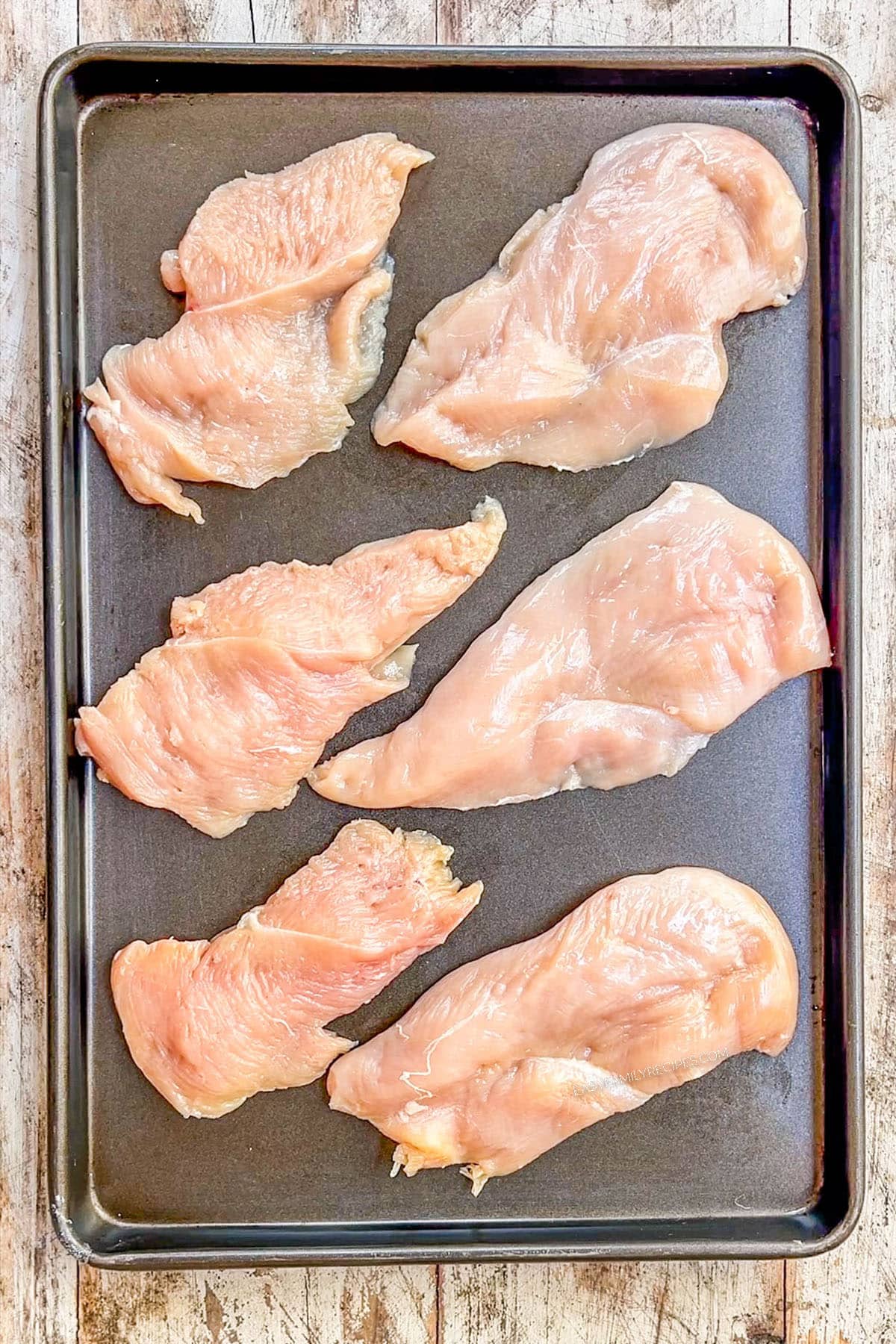 A top view of thin chicken breasts being laid on a baking sheet, step 2 in making Monterey Jack Unfried Chicken