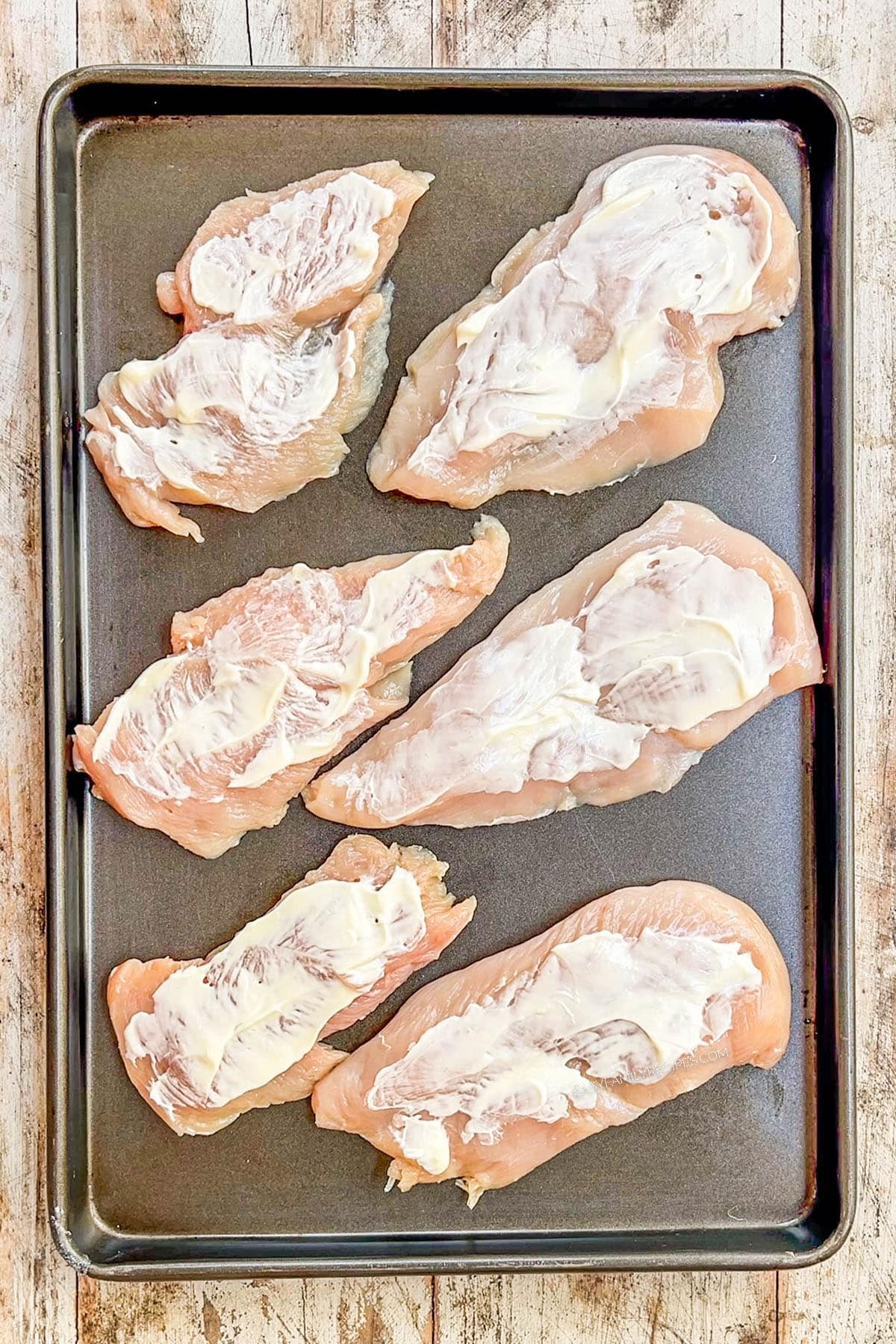 A top view of Monterey Jack Unfried Chicken being made. This step involves spreading a thin layer of mayo over the chicken.