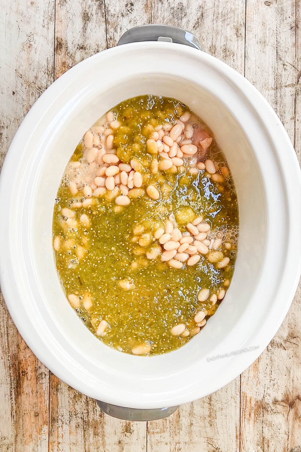 A top view of a white Crock Pot with salsa being added for Salsa Verde Chicken Soup being added; step 3 of making the soup.