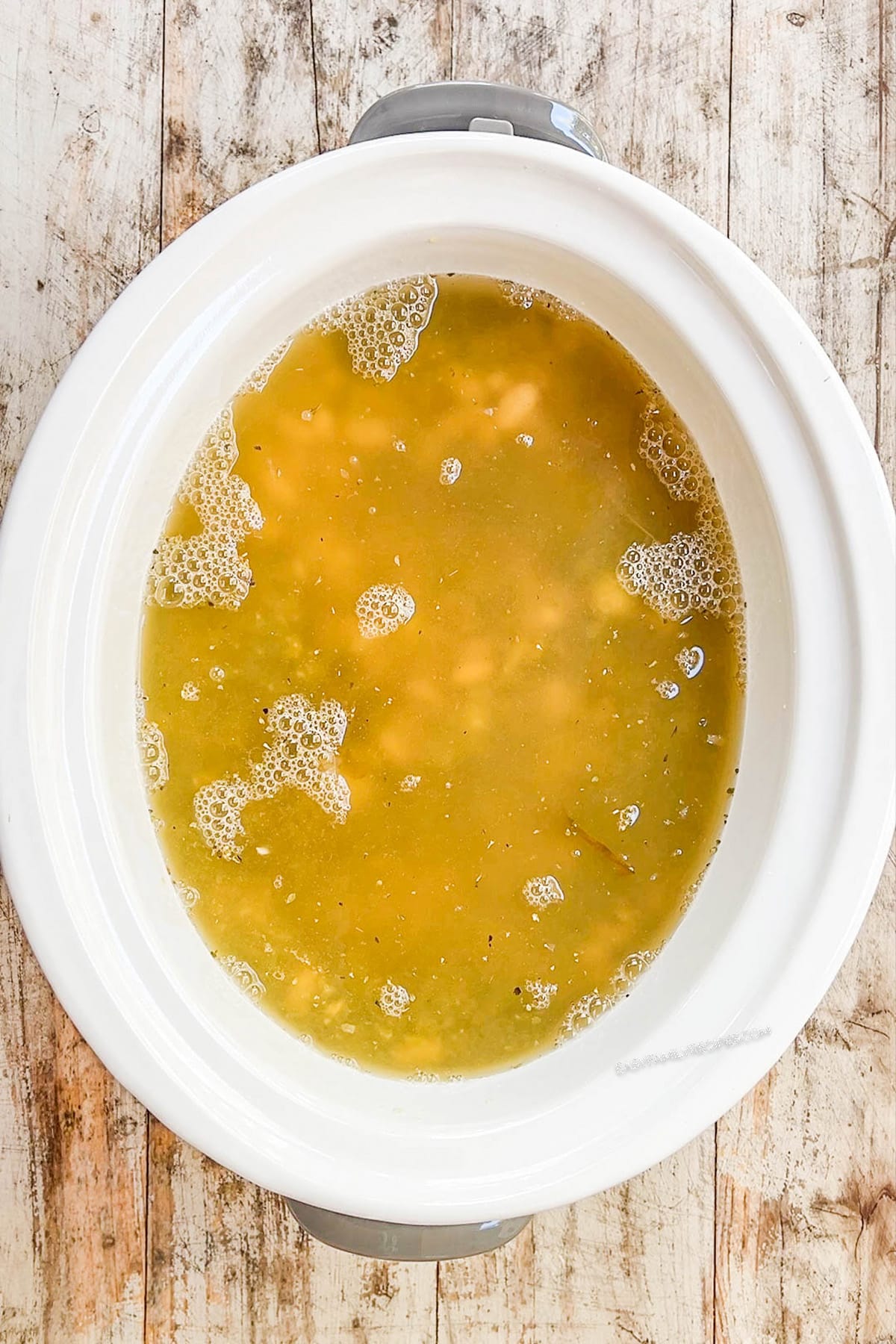 A top view of a white Crock Pot with broth being added for Salsa Verde Chicken Soup being added; step 4 of making the soup.