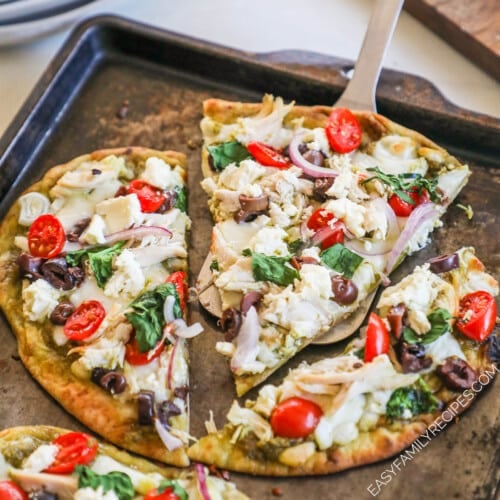 A server lifts a slice of Mediterranean Flatbread off of the baking sheet.