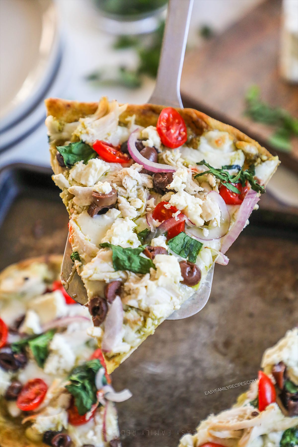 A server lifts a slice of Mediterranean Flatbread off of the baking sheet.