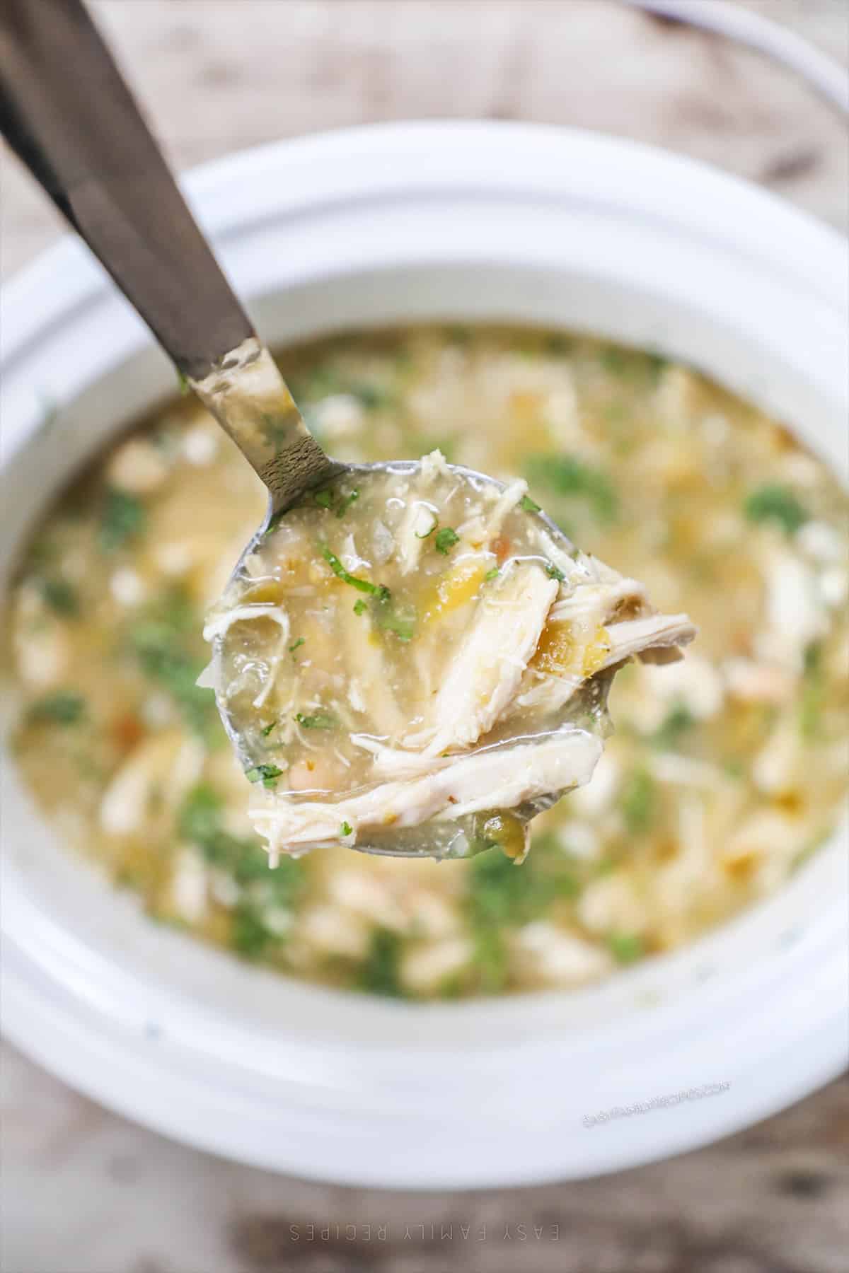 A white bowl of Salsa Verde Chicken Soup with a spoonful of the soup being lifted out of the bowl.