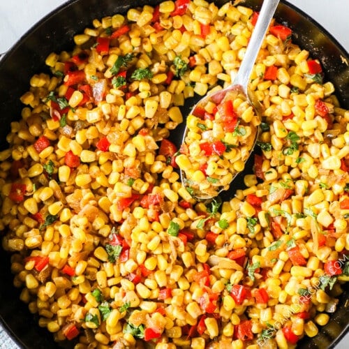 Southwest corn in a skillet with a spoon scooping out a serving.