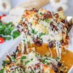 A gold spatula in a white casserole dish that is filled with baked Tuscan Garlic Chicken.