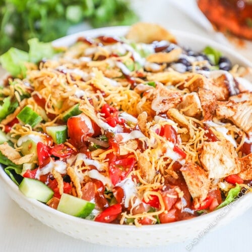 BBQ Chicken Ranch Salad in a white bowl with cilantro and more BBQ chicken in the background.