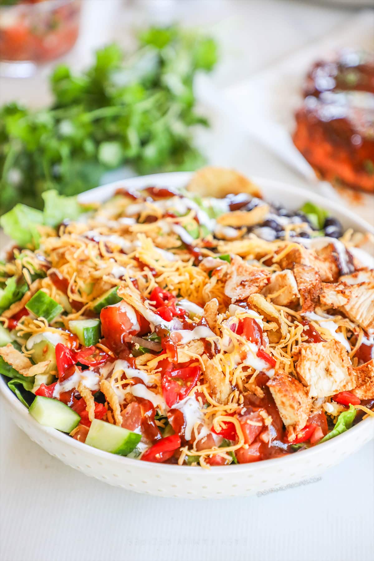 BBQ Chicken Ranch Salad in a white bowl with cilantro and more BBQ chicken in the background. 