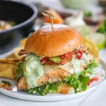 Baja Chicken Sandwich on a white plate with a skillet and ingredients in the background.