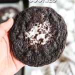 A hand holding a chocolate marshmallow cookie with more cookies on a dark-colored baking sheet in the background. The text reads, “Chocolate Marshmallow Cookies.”