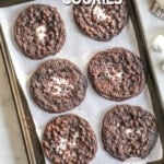 A top view of a dark silver baking sheet lined with parchment paper, and six chocolate marshmallow cookies. The text reads, “Chocolate Marshmallow Cookies.”