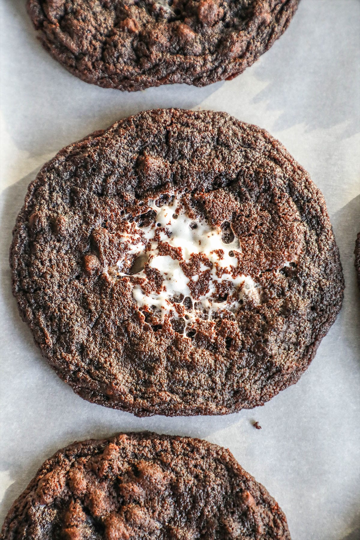 A close-up of a chocolate marshmallow cookie sitting on a parchment paper liner.