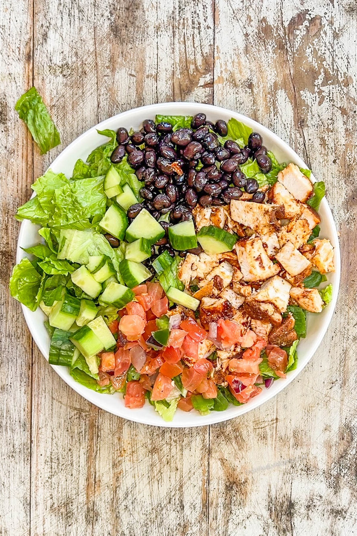 Step 2 of making BBQ Chicken Ranch Salad. The salad is assembled in a white bowl on a distressed wood background.