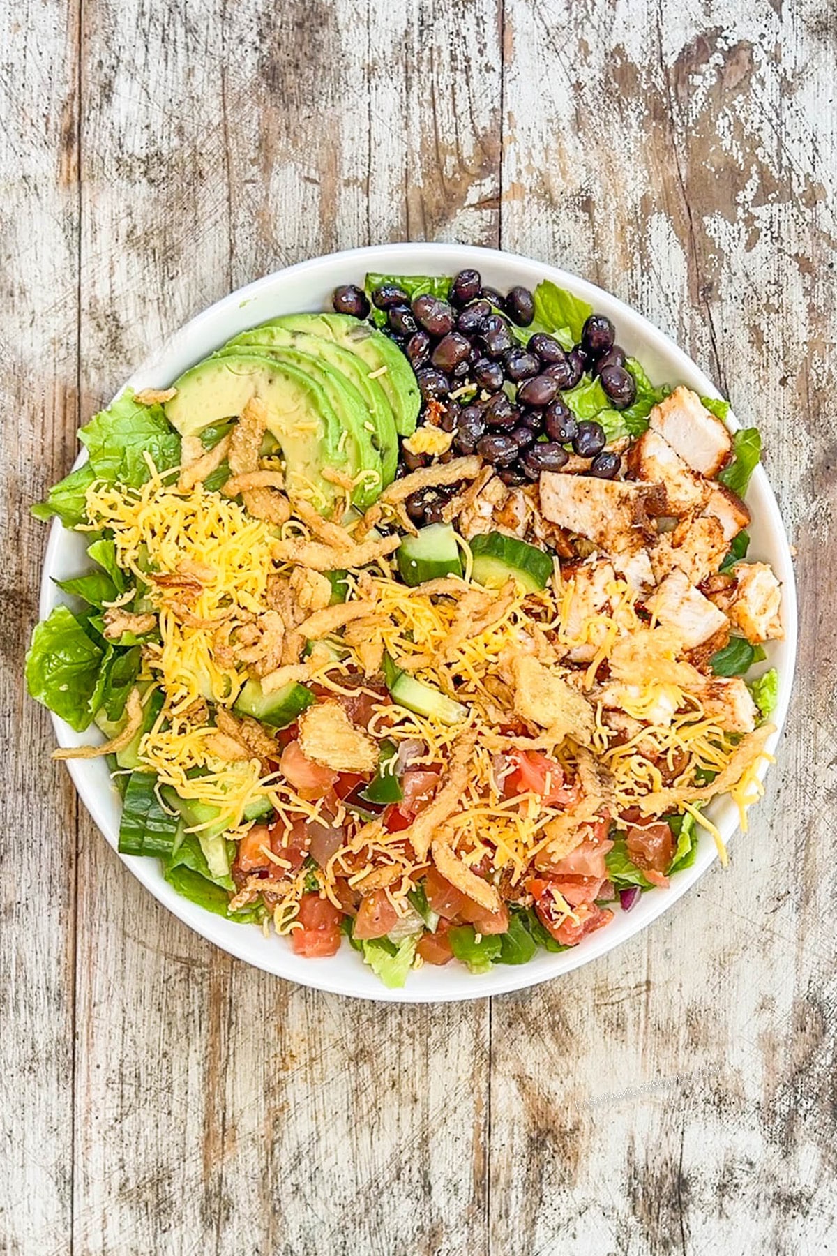 Step 3 of making BBQ Chicken Ranch Salad. The salad is assembled in a white bowl on a distressed wood background.