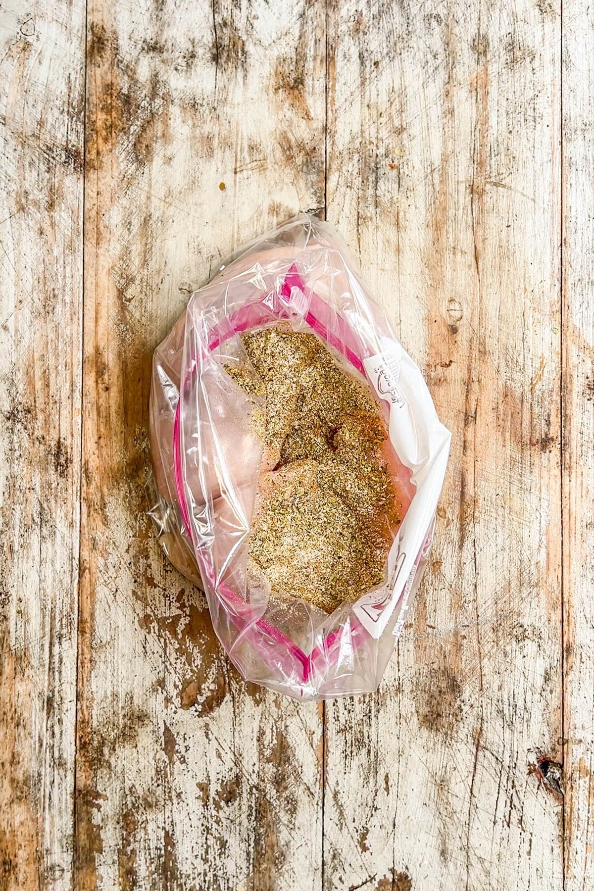 Chicken is seasoned and placed in a zip-top bag on a distressed wood background, step one for making Baja Chicken Sandwiches.