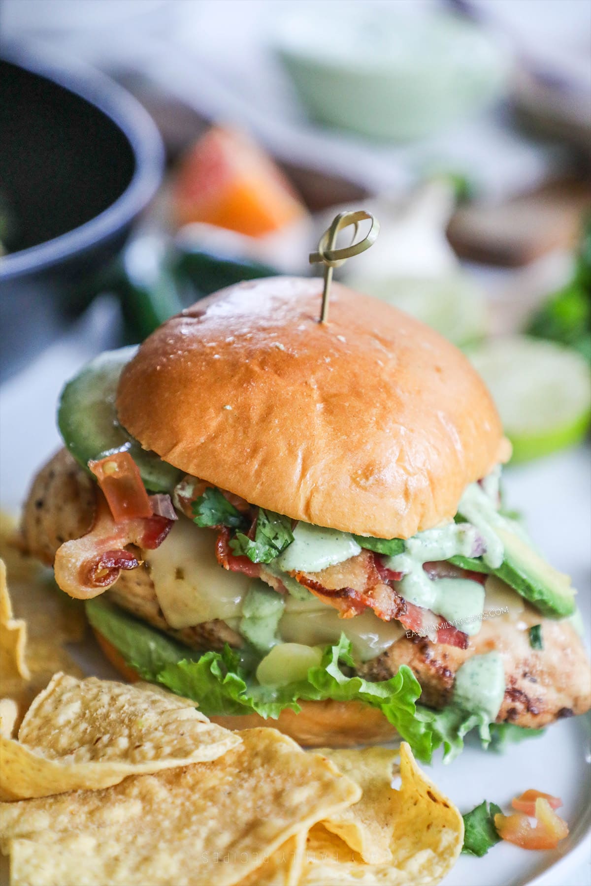 Baja Chicken Sandwich on a brioche bun with chips in the foreground. A skewer holds the sandwich together.