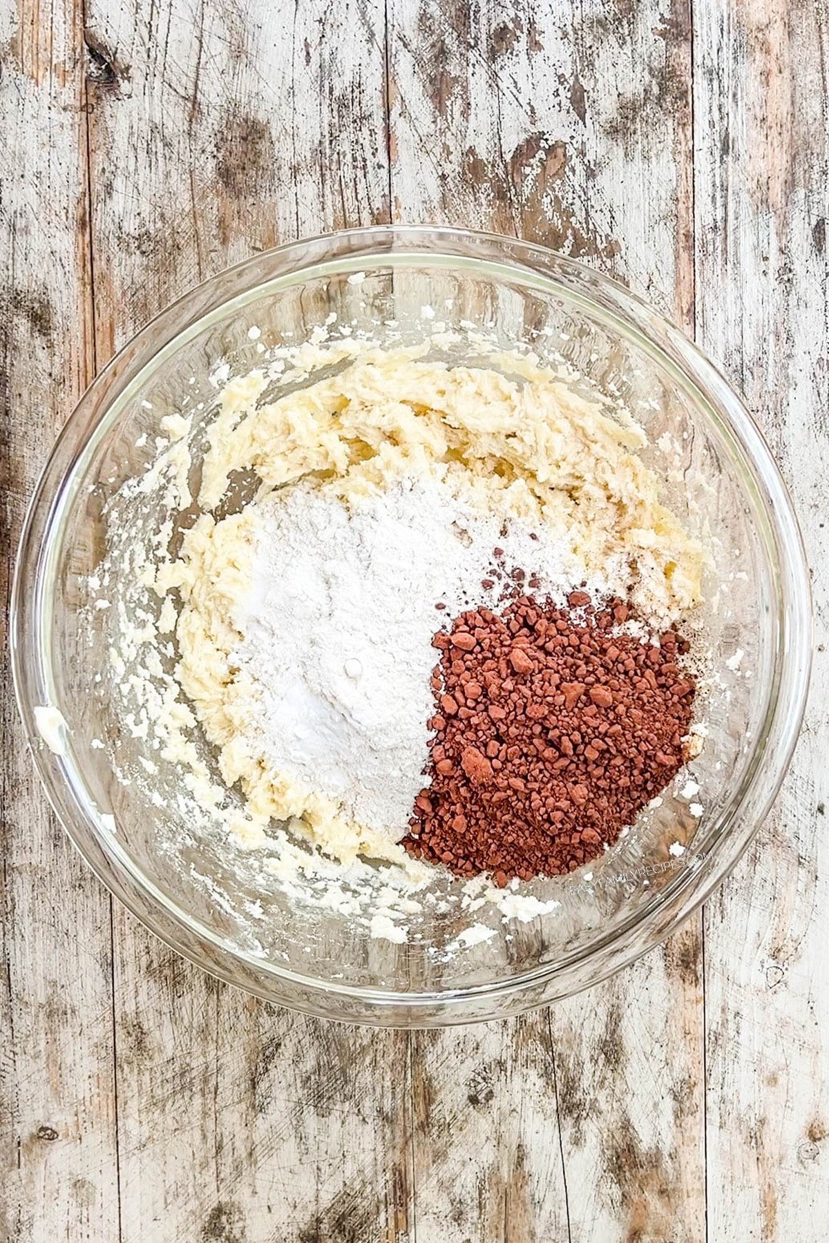 Step 3 for making chocolate marshmallow cookies: The dry ingredients are added to a glass bowl full of the wet dough ingredients.