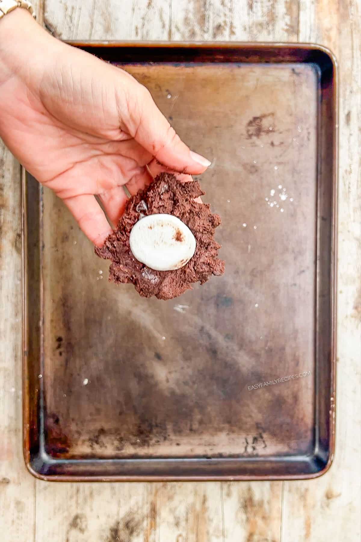 Step 5 for making chocolate marshmallow cookies: A marshmallow is placed into the center of the cookie dough.