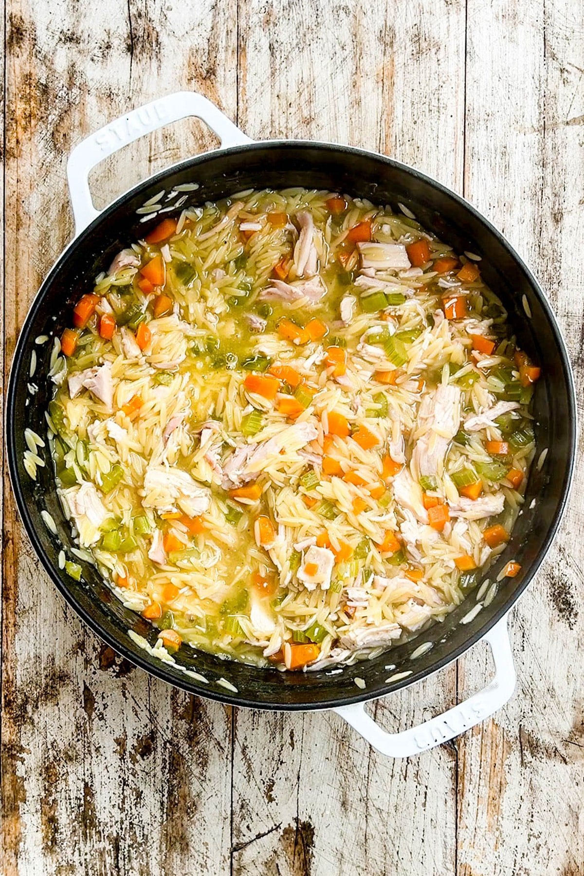 Creamy Lemon Chicken Orzo Soup in a white Dutch oven with a distressed wood background.