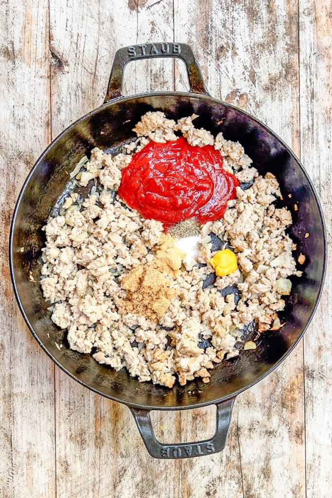 ground chicken in a skillet toopped with ketchup, brown sugar, and mustard.