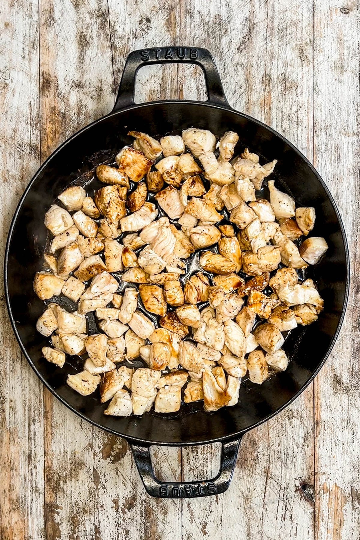 Step 3 of making Hibachi Chicken: Chicken cooks in a black skillet on a distressed wood background.