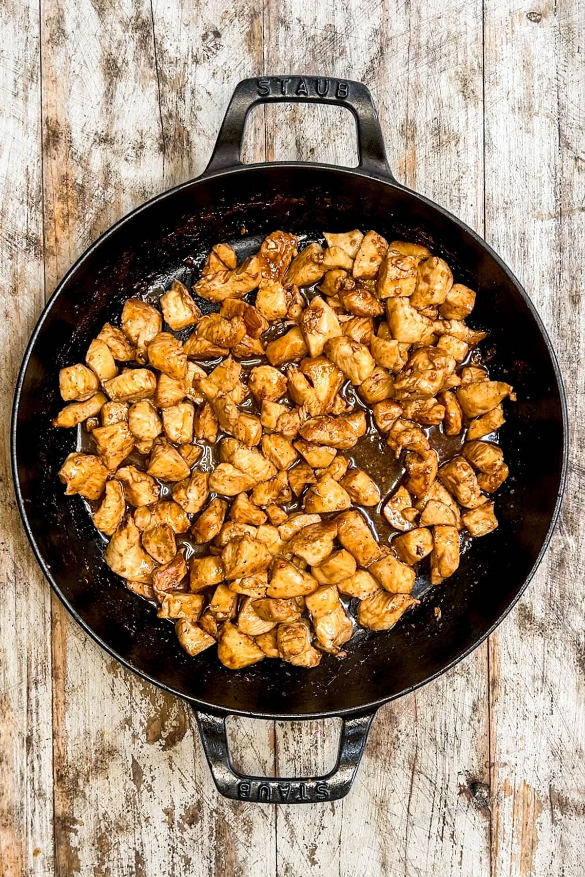 Step 4 of making Hibachi Chicken: Golden seared cooked chicken in a black skillet on a distressed wood background.