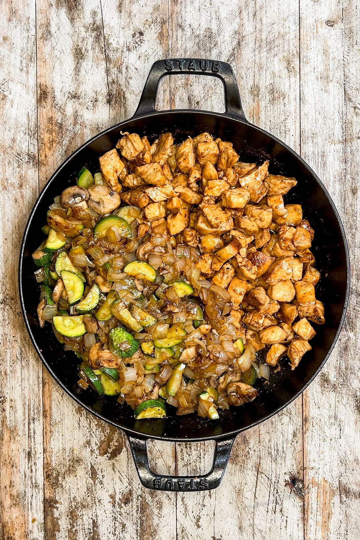 Step 5 of making Hibachi Chicken: Chicken, veggies, and rice in a black skillet on a distressed wood background.