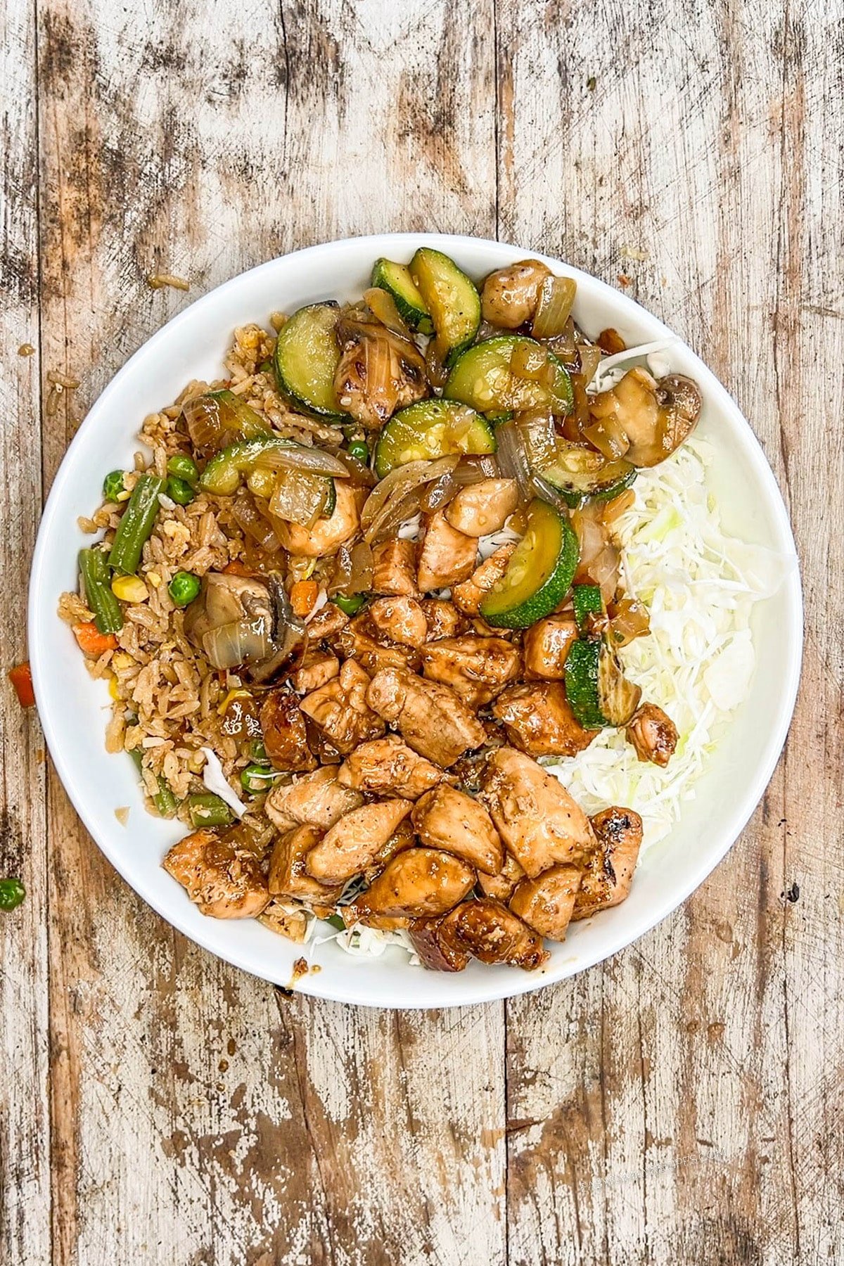 Step 6 of making Hibachi Chicken: A serving of Hibachi Chicken & vegetables on a white plate on a distressed wood background.