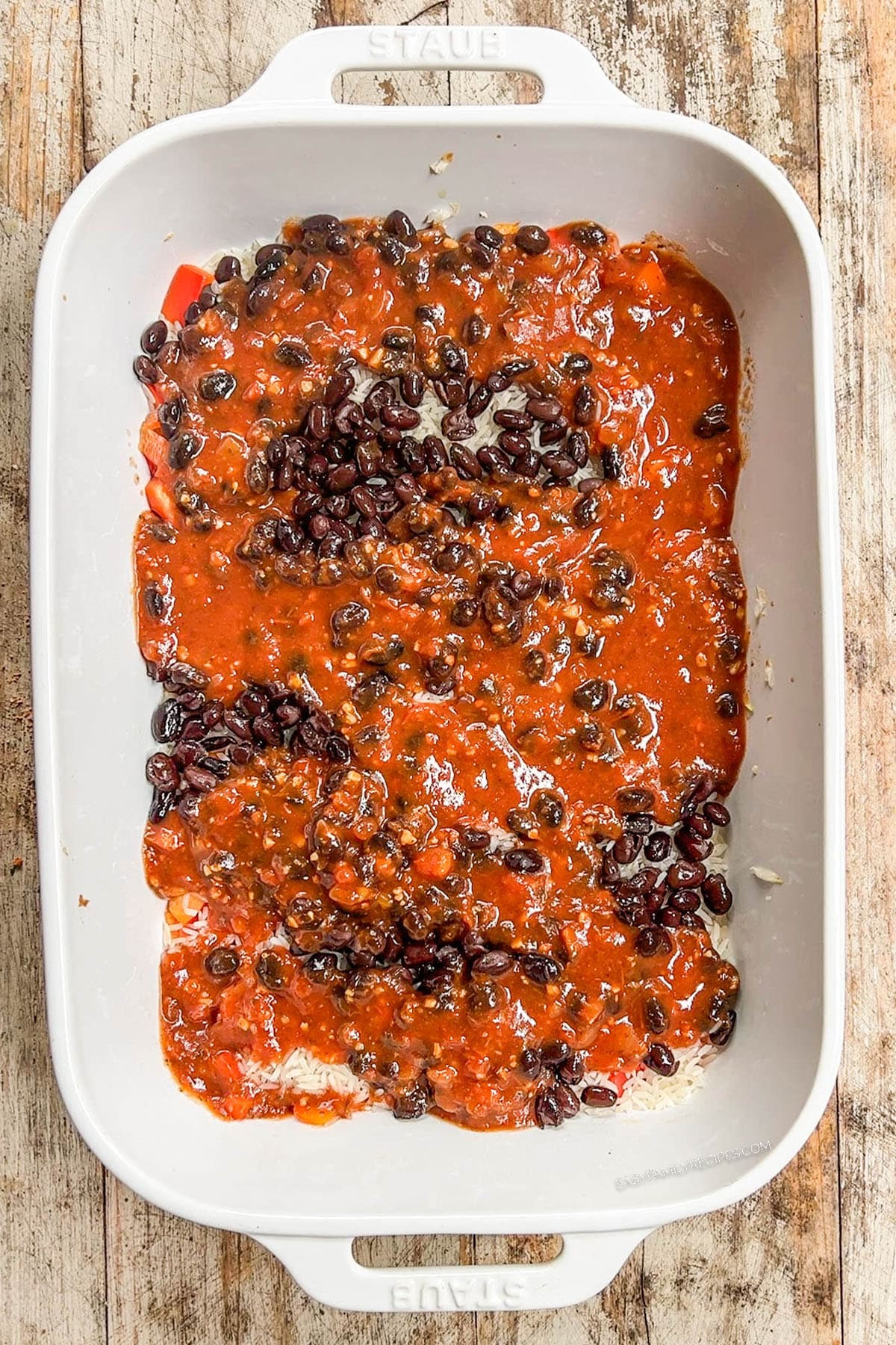 Step 3 of how to make Mexican Chicken & Rice Bake: Beans and tomatoes are added to the white casserole dish.