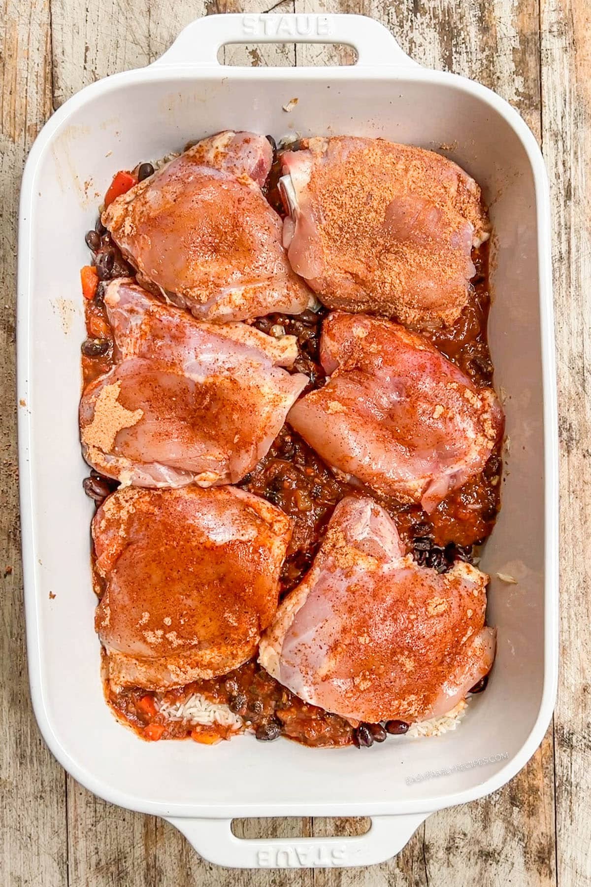 Step 4 of how to make Mexican Chicken & Rice Bake: Chicken thighs are added and hot broth is poured over the top.