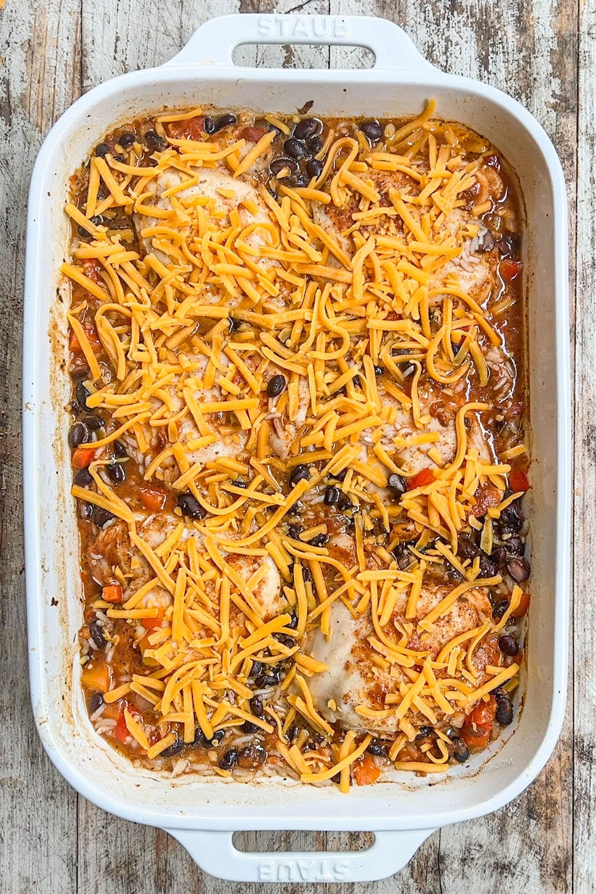 Step 5 of how to make Mexican Chicken & Rice Bake: Cheese is sprinkled over the top of the chicken thighs, rice, veggies, and broth.