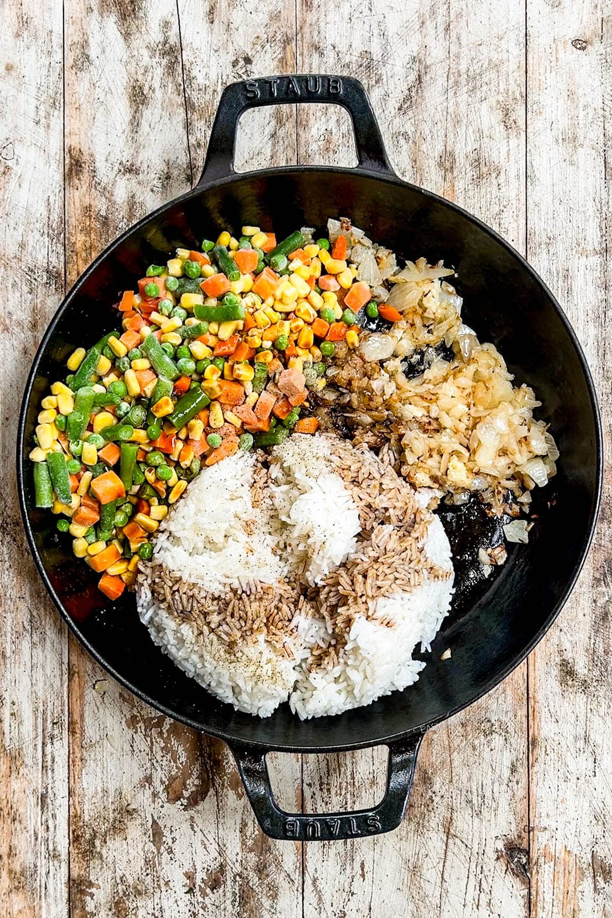 Veggies and seasonings are added to a skillet for vegetable fried rice.