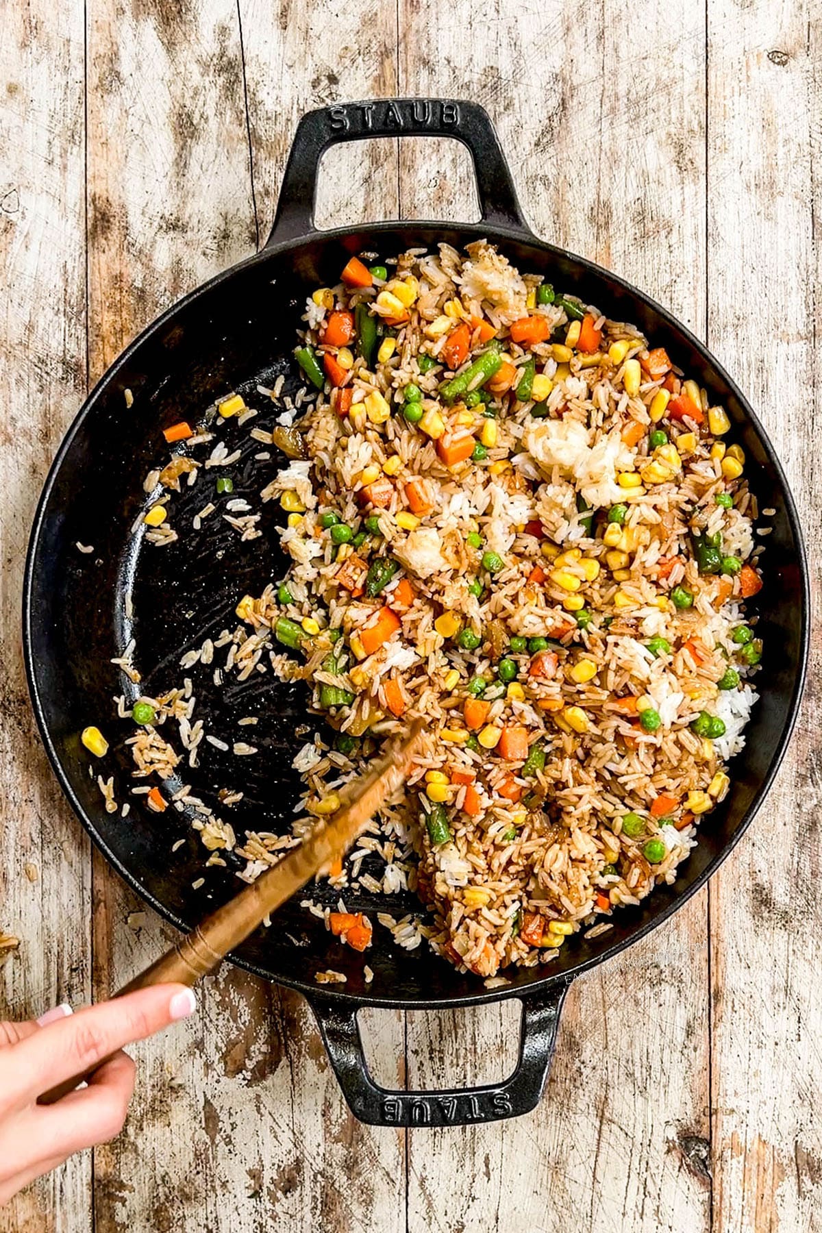 Ingredients for vegetable fried rice are stir-fried in a black skillet.