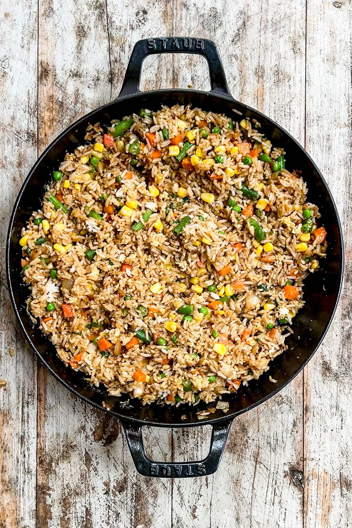 Vegetable fried rice in a black skillet on a distressed wood background.