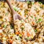 A black skillet full of vegetable fried rice, with a wooden spoon in it. The text reads, “Vegetable Fried Rice.”