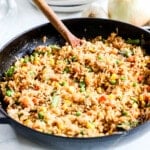 vegetable fried rice in a black skillet on a white background. A wooden spoon is in the rice.