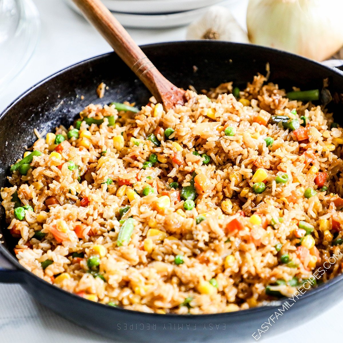 vegetable fried rice in a black skillet on a white background. A wooden spoon is in the rice.