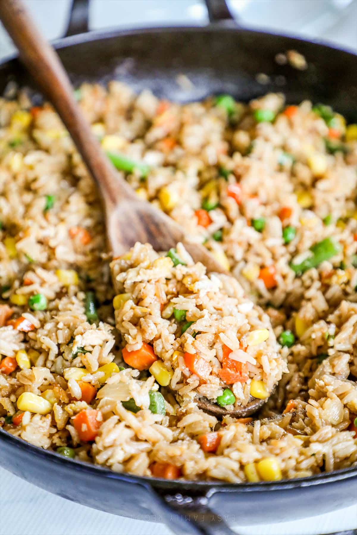 A black skillet full of vegetable fried rice, with a wooden spoon in it. 