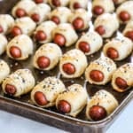 Mini pigs in a blanket lined up on a sheet pan