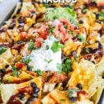 BBQ chicken nachos with sour cream, pico de Gallo, and cilantro on top. The text reads, “BBQ Chicken Nachos”