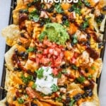 A sheet pan full of BBQ chicken nachos with assorted toppings. The text reads, “BBQ Chicken Nachos”